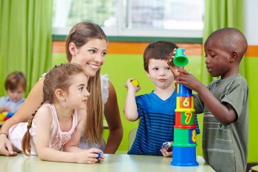 Children,With,Nursery,Teacher,Building,Tower,In,A,Kindergarten,Group