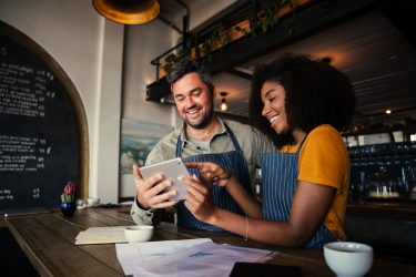 Manager,And,Waitress,Laughing,At,Designs,On,Digital,Tablet,Standing