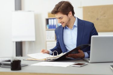 Young,Businessman,Working,With,Documents,Looking,Through,Papers,In,Folder,